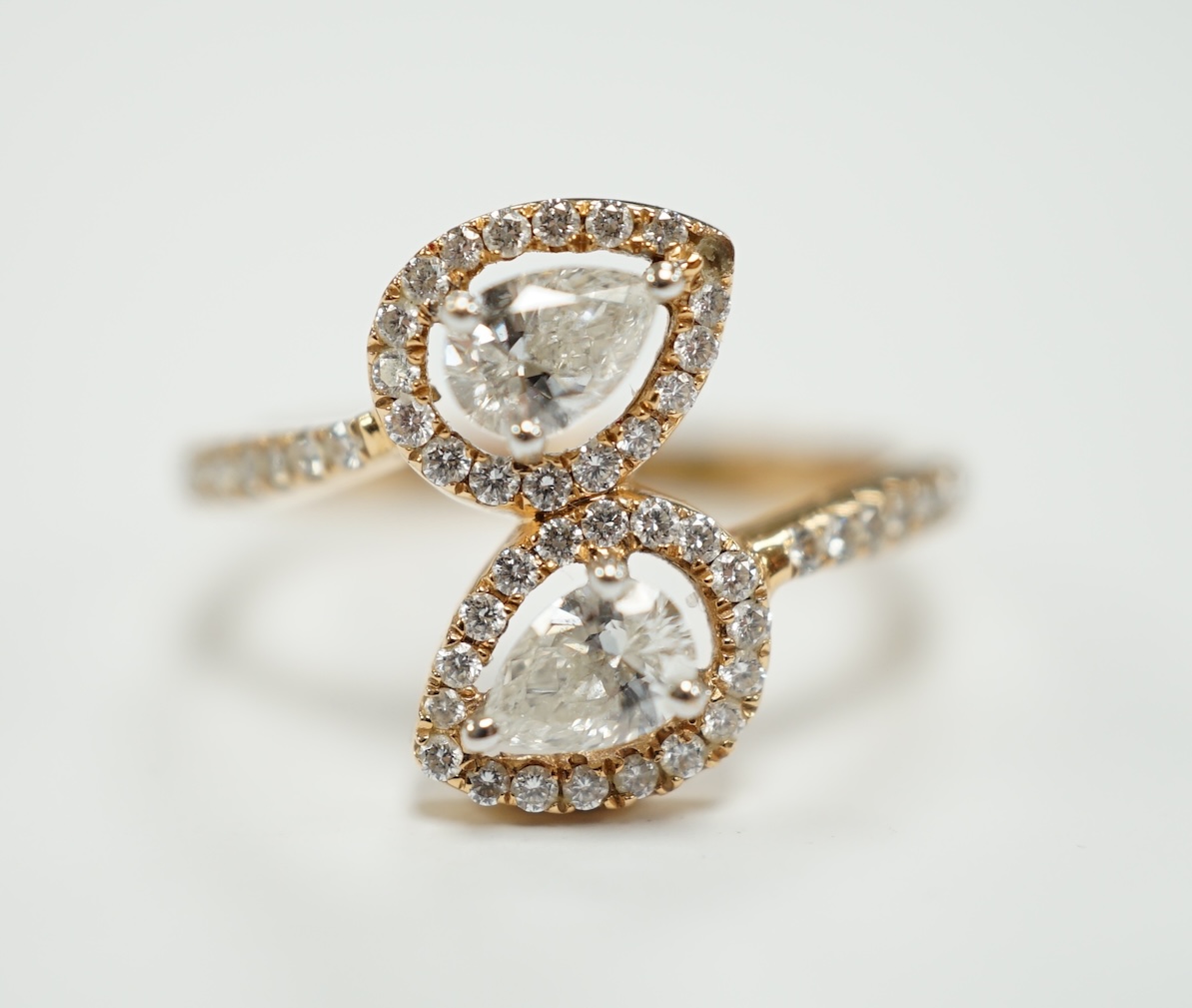 A modern 18k and two stone pear cut diamond set cross-over ring, with diamond chip border and shoulders, size L, gross weight, 2.9 grams.